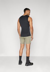 Must musta varrukateta ülemine osa, mis on keha järgnev, kombineeritud roheliste lühikeste pükstega; esineb taskuid ja nähtavaid õmblusi; kantud mustade sokkide ja jalanõudega.