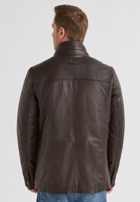 Braune Lederjacke mit Stehkragen, glatter Textur und dezenten Steppdetails. Die Rückansicht zeigt ein Logo-Patch und geknöpfte Bündchen.