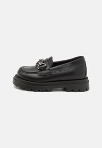 Mocasines de cuero negro con suela de goma gruesa, que presentan un hebilla metálica decorativa en la parte frontal y detalles de costura visibles.