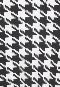 Czarna i biała tkanina w wzór houndstooth z ząbkowanymi, powtarzającymi się kształtami geometrycznymi tworzącymi klasyczny deseń tekstylny.