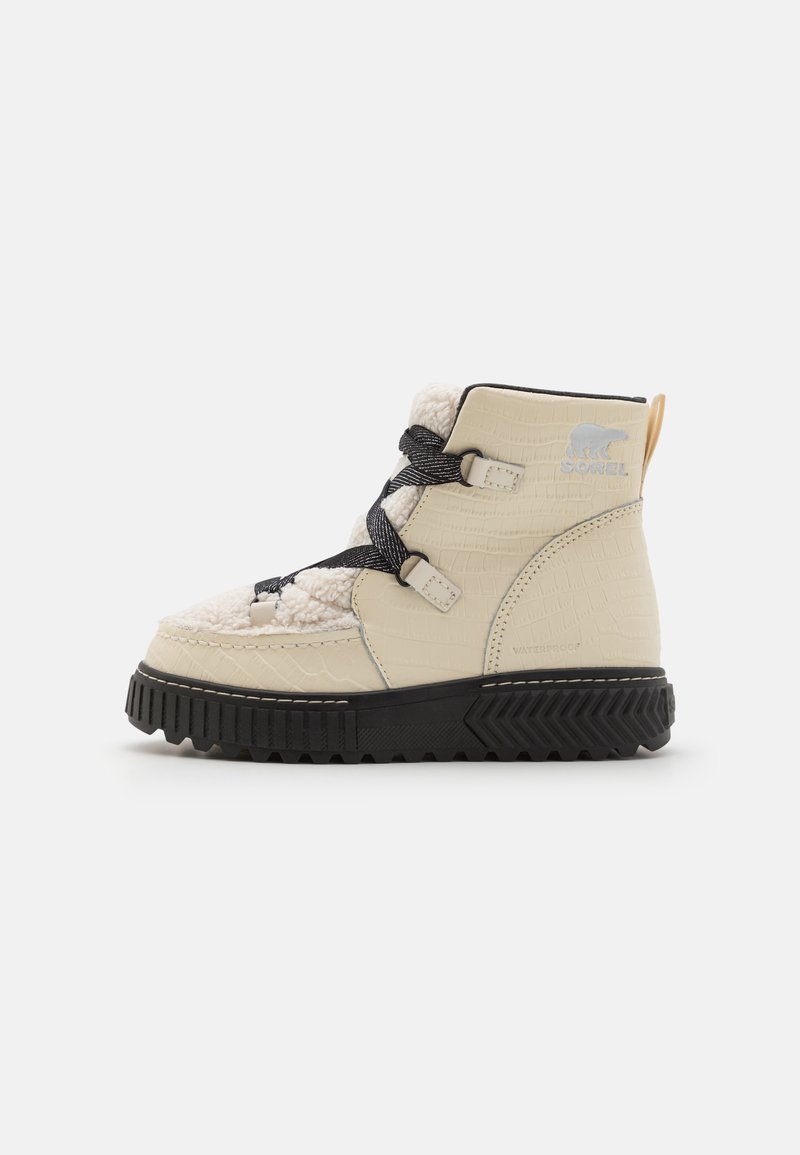Beige mid-top støvel med en teksturert krokodillelignende finish, svart gummisåle, svarte lisser og en bakre trekkflik. Vannavvisende design.