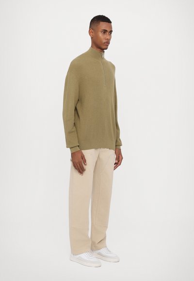 Olive green zip-up sweater with a high collar, paired with beige wide-leg pants and white sneakers. Smooth texture and loose fit.