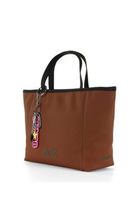 Brązowa torebka tote z faux skóry z czarnymi akcentami, wyposażona w podwójne uchwyty i kolorowy brelok. Z wyróżniającym się logo z przodu.