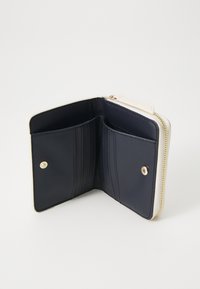 Portefeuille en cuir marine avec des accents crème, doté d'une fermeture éclair, de plusieurs emplacements pour cartes et d'un compartiment pour les pièces ou les billets. Détail en métal doré.