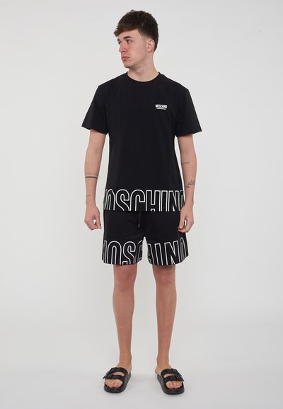 Set di t-shirt nera e pantaloni shorts con grande scritta bianca "MOSCHINO". Realizzato in tessuto morbido, con maniche corte e vestibilità rilassata. Vita regolabile.