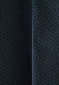 Gros plan sur un tissu texturé bleu foncé avec une couture verticale au centre, montrant un motif ressemblant à du tricot des deux côtés.