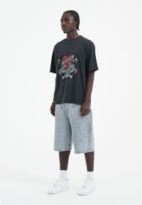 Černé grafické tričko s potiskem lebky a srdce v kombinaci se světlými modrými džínovými kraťasy. Bílá sneaker obuv dokončuje celkový vzhled.