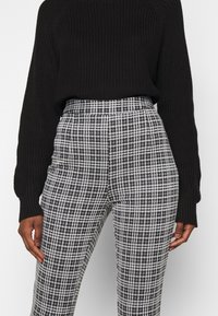 Svart stickad tröja i kombination med högmidjade rutiga byxor i svart och vitt. Byxorna har en åtsittande design med en platt linning och slät textur.