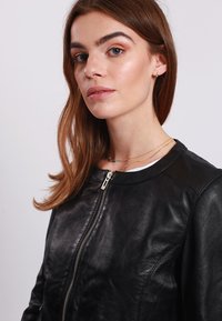 Black leather bomber jacket with a zip front, round neckline, and smooth texture. Features a fitted design and subtle stitching details.