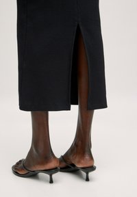 Schwarze geribbelte Midi-Rock mit Schlitz hinten, kombiniert mit schwarzen Absatzsandalen. Der Rock zeichnet sich durch eine glatte Textur und eine taillierte Passform aus.