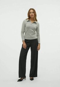 Polo de manga longa cinza-claro com gola, combinado com calças largas pretas com riscas e sapatos pretos de bico fino.