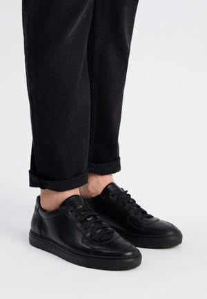 Czarne skórzane sneakersy z sznurowaniem, gładka tekstura, zaokrąglony czubek i gumowa podeszwa, zestawione z podwiniętymi ciemnymi dżinsami.