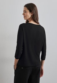 Czarna bluzka z trzyczwartowymi rękawami i okrągłym dekoltem. Gładka faktura, dopasowany fason oraz subtelne marszczenia przy rękawach.