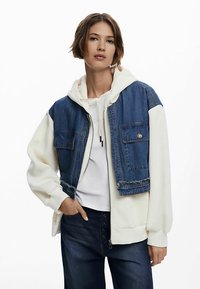 Jachetă din denim și fleece cu design cropt, corp superior din denim albastru, mâneci din fleece alb și două buzunare frontale. Închidere cu fermoar.