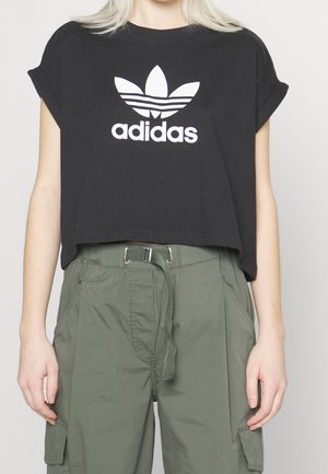 Osoba nosząca czarną krótką koszulkę Adidas oraz luźne oliwkowo-zielone spodnie typu cargo z materiałowym paskiem.