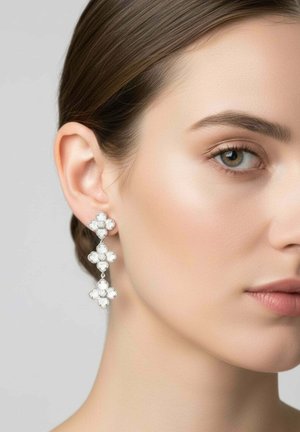 Nő jobb fülének háromrétegű, virág alakú, fehér drágakőből készült, lógó fülbevalóval, semleges háttér előtt.