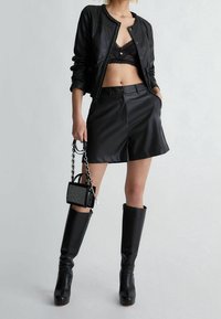 Czarna skórzana kurtka bomberka, czarny koronkowy krótki top, czarne krótkie spodenki z wysokim stanem, sięgające do kolan czarne botki oraz mała czarna torebka na łańcuszku.