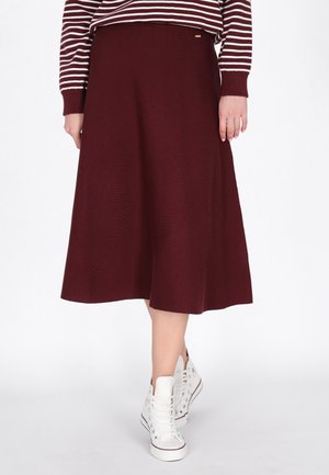 Modelo con una falda midi burdeos de línea A, un jersey de rayas y zapatillas altas blancas, sobre un fondo blanco liso.