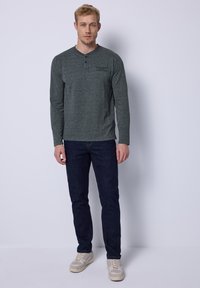 Langarm-Henley-Shirt in Grau mit Knopfleiste, kombiniert mit dunkelblauen Jeans und hellen Sneakers. Glatte Stoffoberfläche.