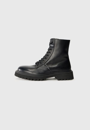 Bottes en cuir noir à lacets avec une tige haute, bout rond, semelle en caoutchouc robuste et détail de logo sur le côté. Œillets en métal ajustables.