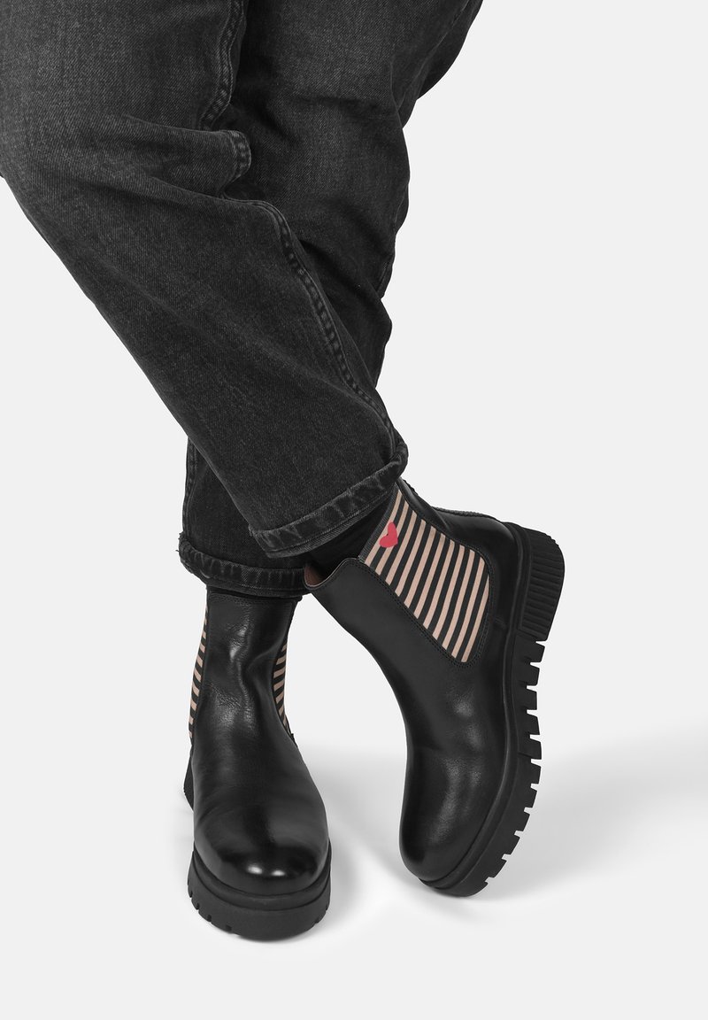 Czarne skórzane botki za kostkę z grubą podeszwą i paskami elastycznymi w pasy po bokach. Skarpety mają mały czerwony detal w kształcie serca.