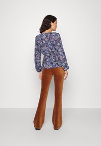 Floral print top in navy with long puffed sleeves, paired with brown corduroy flared pants. The outfit features a fitted silhouette and textured fabric.