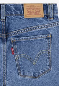 Denim jeans with a light blue color, featuring a leather label on the waistband, back pocket with a red Levi's tab, and yellow stitching.