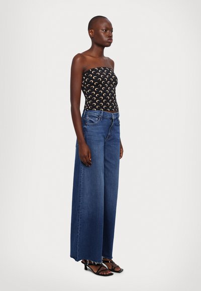 Haut noir sans bretelles avec motif de croissant de lune ; jeans en denim bleu foncé à jambe large avec ourlet effiloché ; sandales à talons noires à lanières.