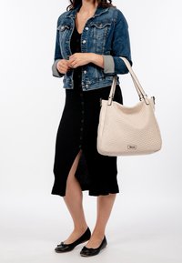 Kremowa pleciona torebka na dwa paski na ramię, zestawiona z dżinsową kurtką na czarnej, prążkowanej sukience z guzikami oraz czarnymi balerinami.