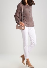 Blouse à manches longues à motifs dans des tons chauds, pantalon blanc fuselé et escarpins nude. Petit sac à main avec une bandoulière chaîne.