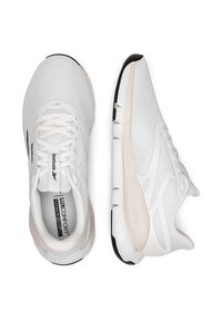 Biele športové topánky s textúrovaným sieťovaným zvrškom, mäkkými béžovými akcentmi a gumovou podrážkou. Obsahuje systém šnurovania a branding na jazyku.