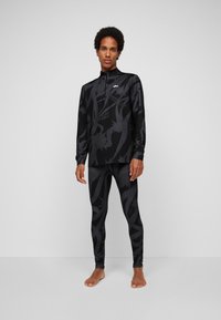 Langärmliges schwarzes Sportshirt und passende Leggings mit einem tonalen, abstrakten Muster. Der Stoff erscheint glatt und eng anliegend.