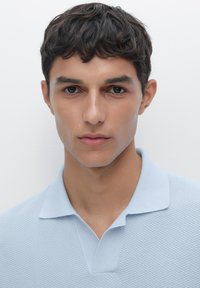 Polo shirt azzurro chiaro con texture e colletto, caratterizzato da un motivo discreto. La maglietta ha maniche corte e una vestibilità comoda.