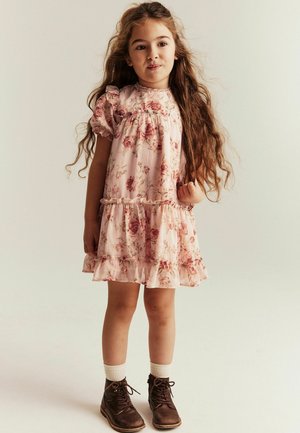Różowa sukienka w kwiaty z bufkami na rękawach, falbankowanym dołem i teksturowaną tkaniną; zestawiona z brązowymi sznurowanymi botkami i białymi skarpetkami.