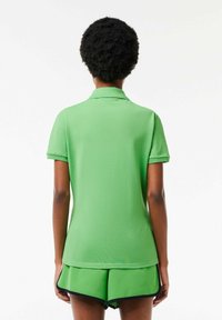 Polo vert à petit col, manches courtes et texture lisse, assorti à un short vert avec une bordure marine.