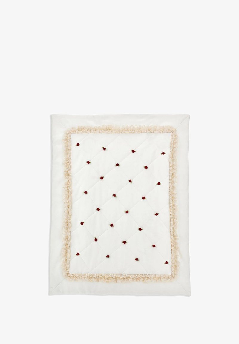 Biała pikowana kołdra z beżowym falbanym wykończeniem i rozsypanymi aplikacjami w postaci czerwonych róż, z diamentowym wzorem na powierzchni.