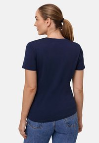 Mørkeblå kortærmet t-shirt med rund hals og glat tekstur, bærer med højtaljede blå jeans. Minimalistisk design, ingen mønstre.