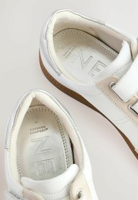 Białe sneakersy z srebrnymi akcentami, z gładką skórzaną cholewką, okrągłym czubkiem, niskim profilem oraz wytłoczonym logo na wkładce.