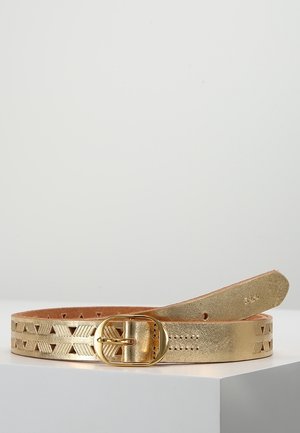 Zlatý kožený pásek s geometrickými výřezy a zaoblenou zlatou sponou ležící na bílém povrchu.