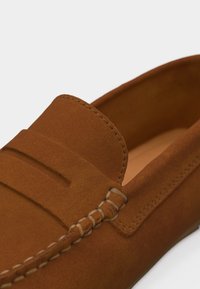 Καφέ μοκασίνι από σουέντ με λεπτομερείς ραφές και εμπρός πάνελ σε στιλ μοκασίνου, σε κοντινή λήψη.