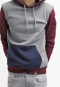 Sweat à capuche gris et bordeaux avec une poche, des cordons et des manches longues bleu marine. Réalisé en tissu doux avec un design en blocs de couleurs.