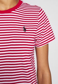 Czerwono-biała, w paski koszulka z okrągłym dekoltem. Posiada haftowane czarne logo po lewej stronie klatki piersiowej. Wykonana z miękkiej bawełny, z krótkimi rękawami.