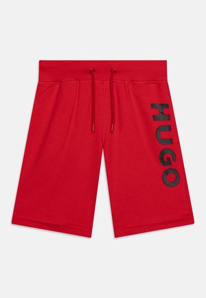 Røde knælange shorts med elastisk talje og snore, med lodret sort "HUGO" tekst på højre ben.