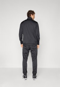 Black athletic jacket and pants set, made of smooth, lightweight fabric with a high collar. Pants have elastic cuffs and pockets.