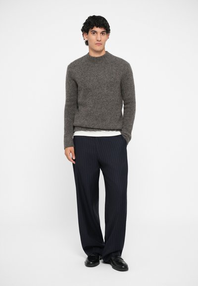 Gray textured sweater with ribbed neckline, layered over a white shirt. Navy pinstriped trousers and black shoes complete the look.