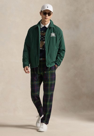 Mees, kes kannab valget nokamütsi ja päikeseprille, rohelist jopet, tumesinist kanda karumotiiviga kampsunit, ruudulisi pükse ja valgeid tenniseid, kõnnib edasi.