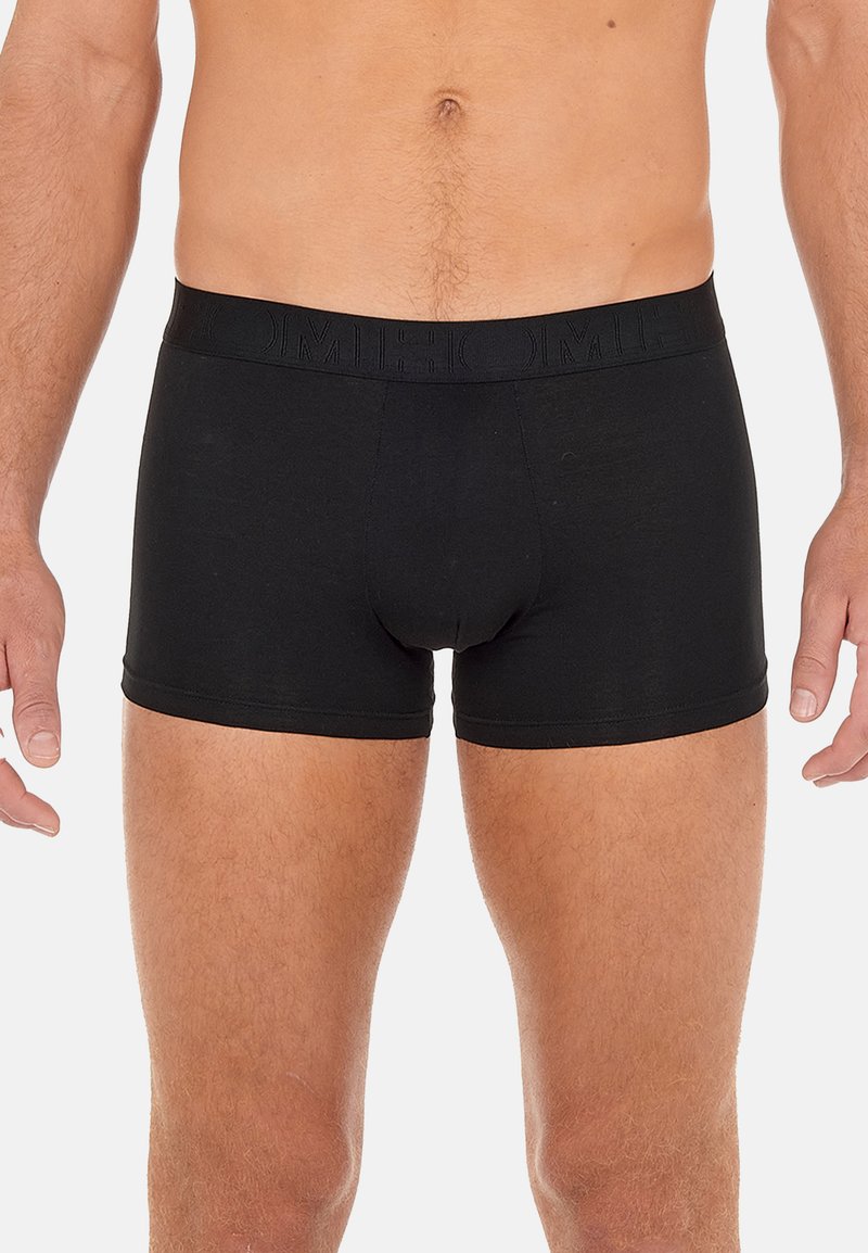 Male torso and upper legs wearing plain black boxer briefs with an elastic waistband, standing against a neutral background.