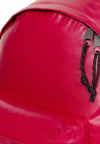 Rode nylon rugzak met een afgeronde bovenkant, voorzien van een gestructureerd oppervlak, zwarte ritsen en zwarte koordaccenten voor het aanpassen.