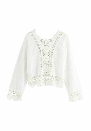Blouse blanche courte à manches longues, présentant des motifs floraux brodés et des détails en dentelle au niveau du col et de l'ourlet.