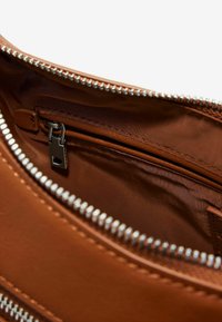 Interno di una borsa in pelle marrone con una tasca con zip dotata di una cerniera metallica argento. La foderatura è di un tessuto marrone liscio, che mette in risalto la forma della tasca.